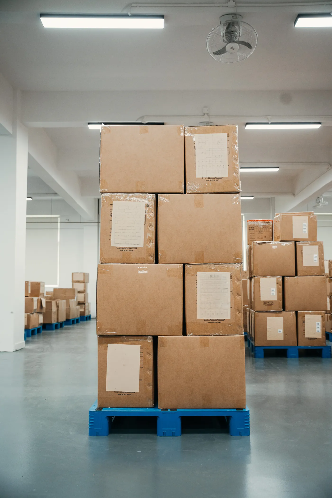 Stack of cardboard boxes on a blue pallet inside a spacious, well-lit warehouse room.