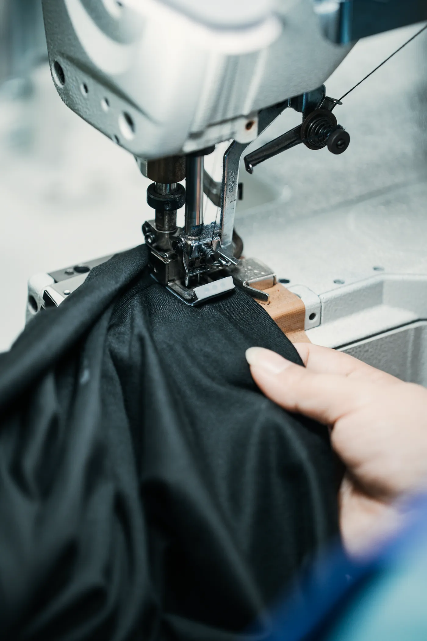 Close-up of a sewing machine stitching black fabric guided by a person's hand.