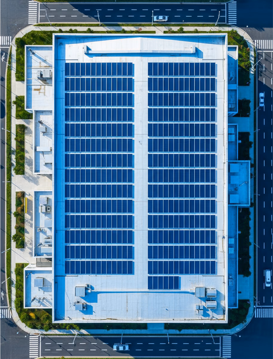Aerial view of a large, flat commercial building roof in New Jersey fully covered with a crisp array of black-frame solar panels; parking lot and suburban streets below
