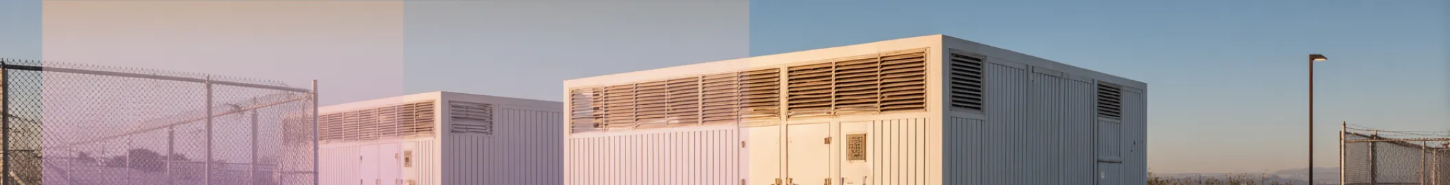 battey storage containers lined up on a large concrete surface under a clear blue sky.