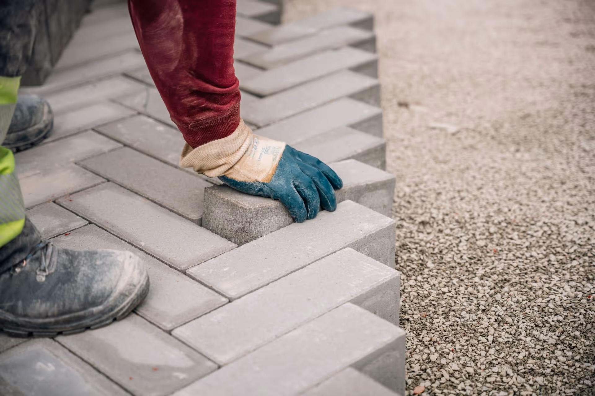 Een arbeider met handschoenen die grijze straatstenen in een visgraatpatroon legt.