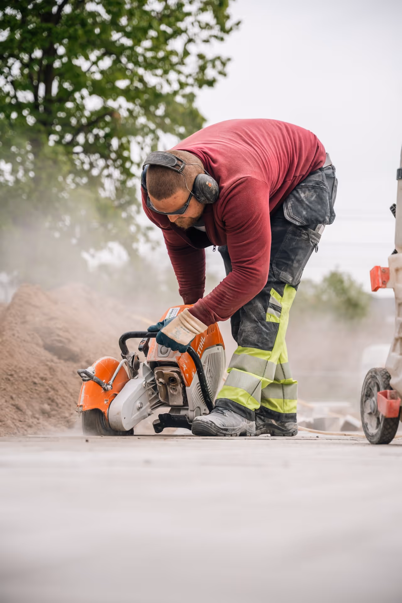 Een bouwvakker met gehoorbescherming die op een bouwplaats beton zaagt met een grote oranje elektrische zaag.