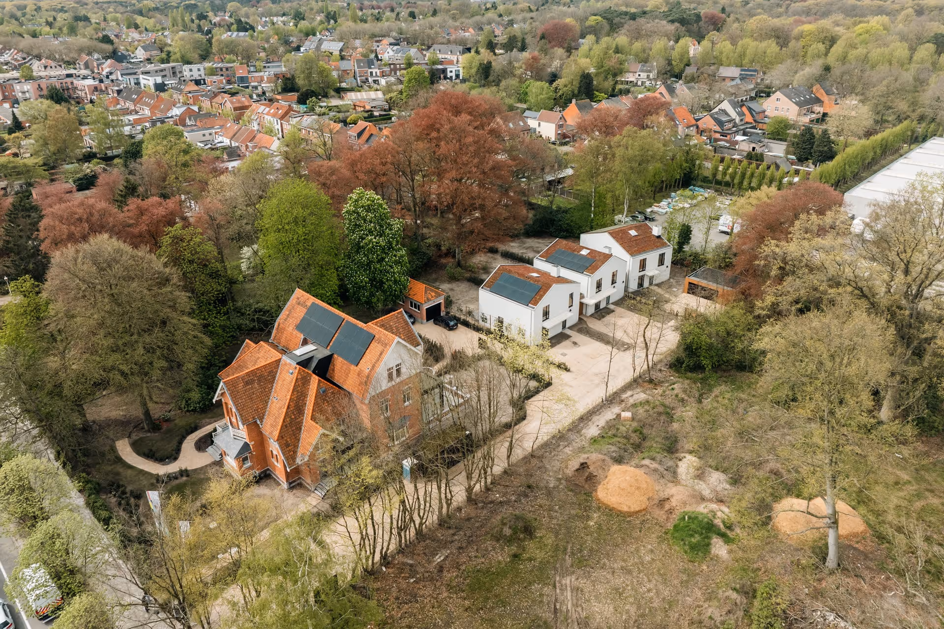 Luchtfoto van een woonwijk met huizen met zonnepanelen op de daken, omgeven door bomen en groen.