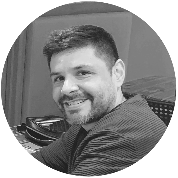 Smiling man with short dark hair and a beard wearing a striped shirt, seated indoors.