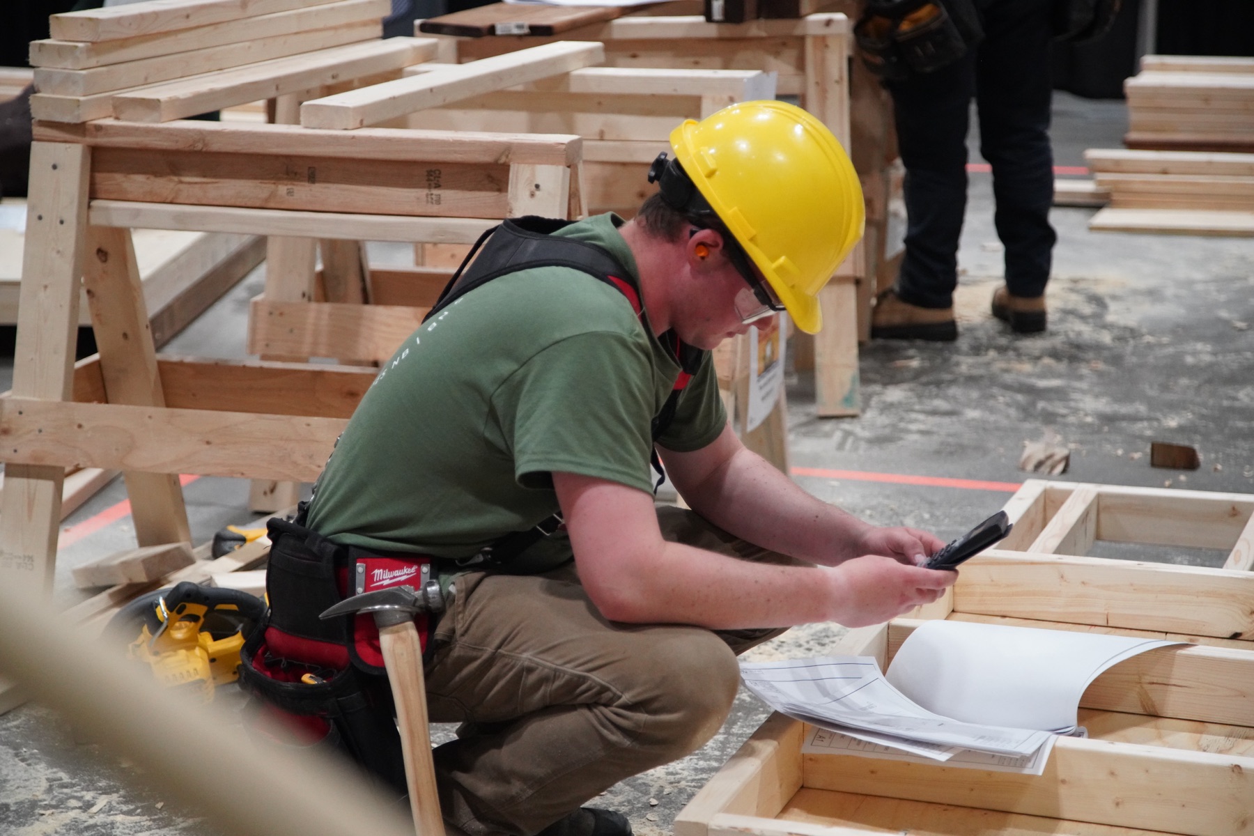 Carpentry competitor reviewing plans inside a framed structure