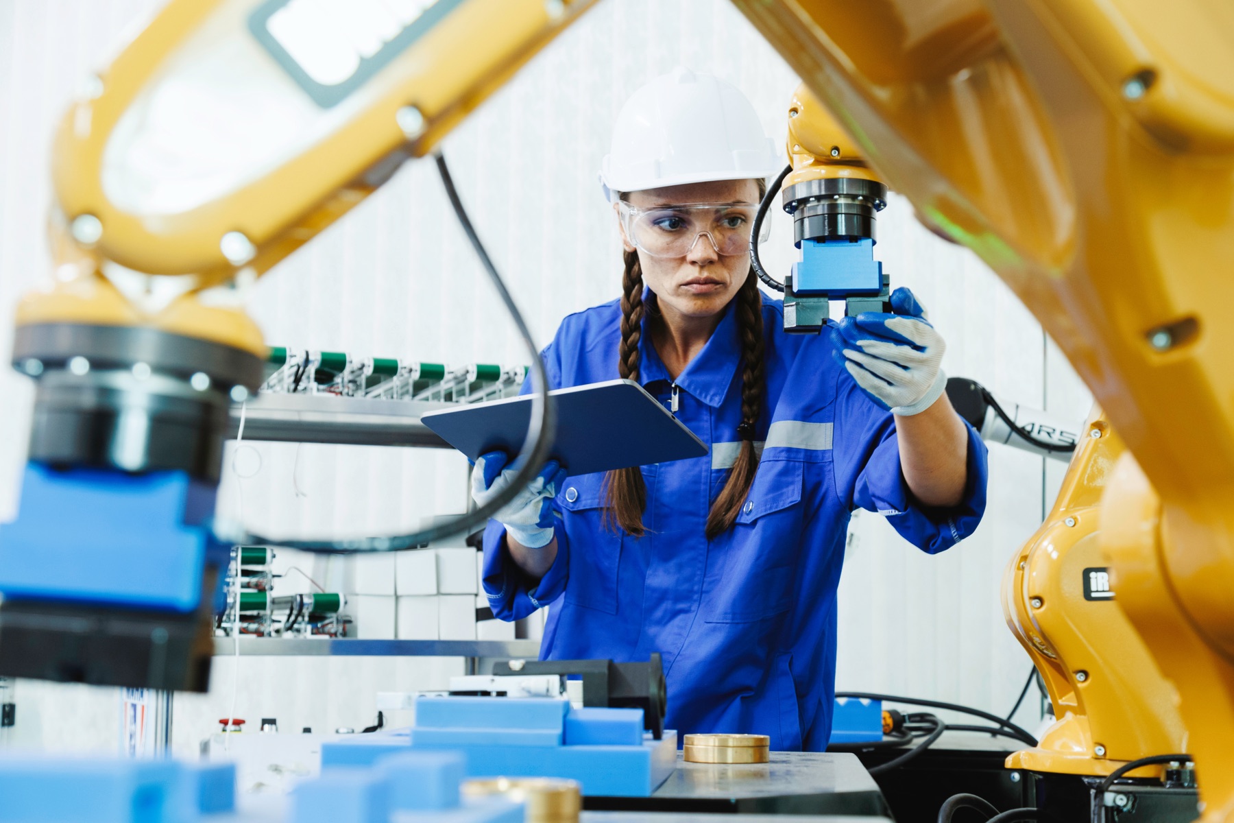 Technician in coveralls and hard hat working with an industrial robotic arm