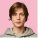 A young person with short brown hair wearing a gray hoodie stands against a solid pink background, looking directly at the camera with a neutral expression.