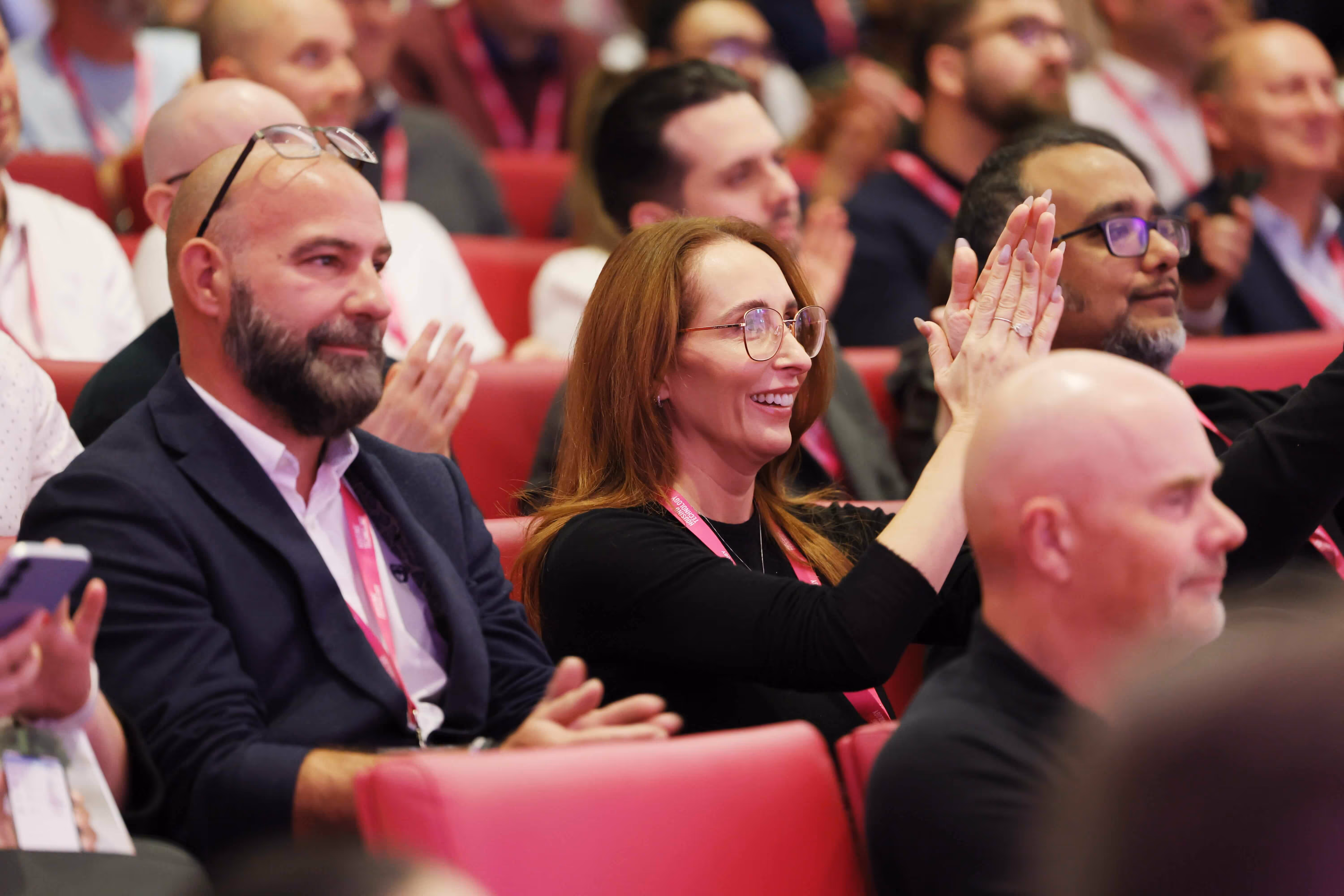 Audience members seated in a conference room clapping and smiling during an event.