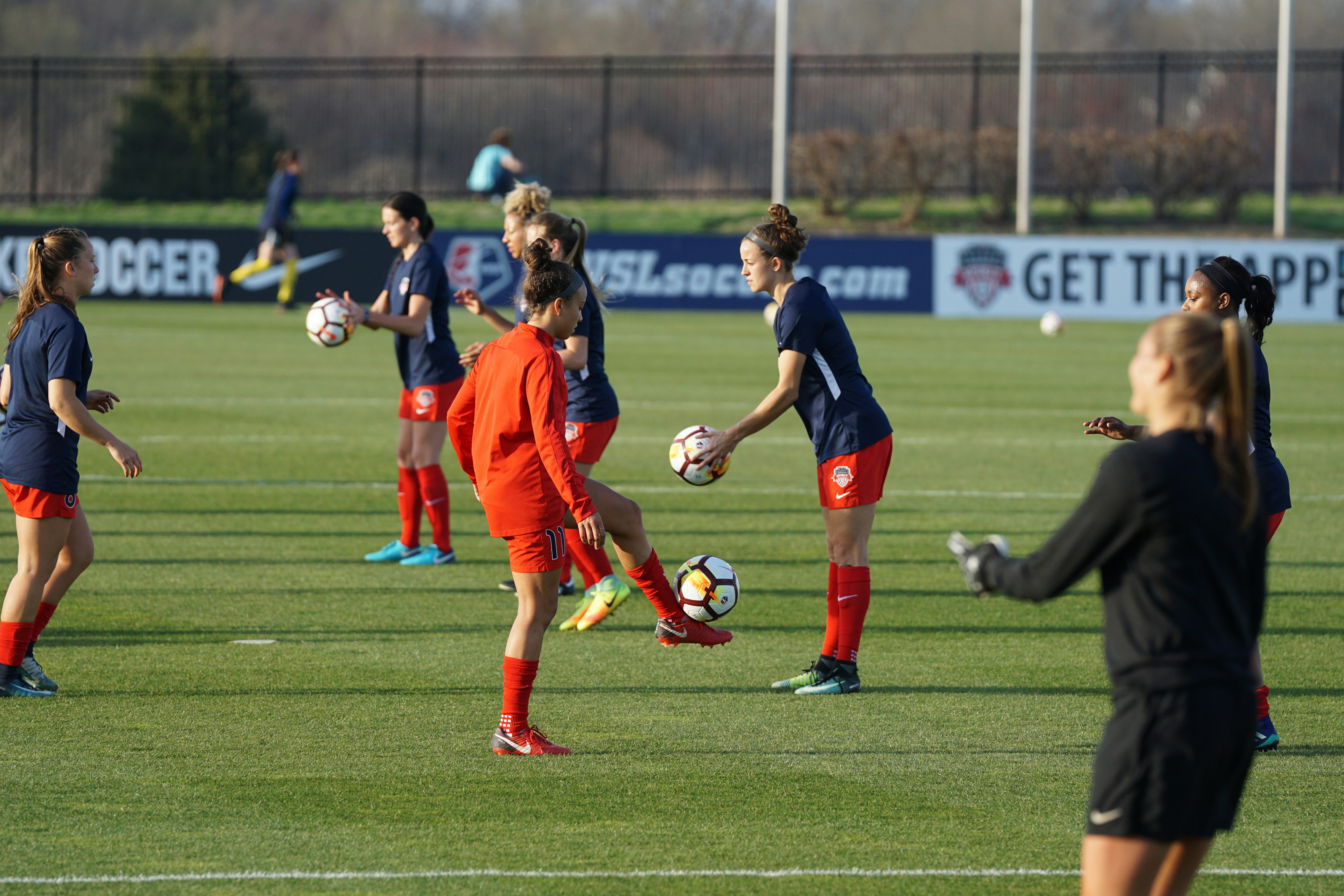 Women soccer players warming up on the field with soccer balls during daylight.