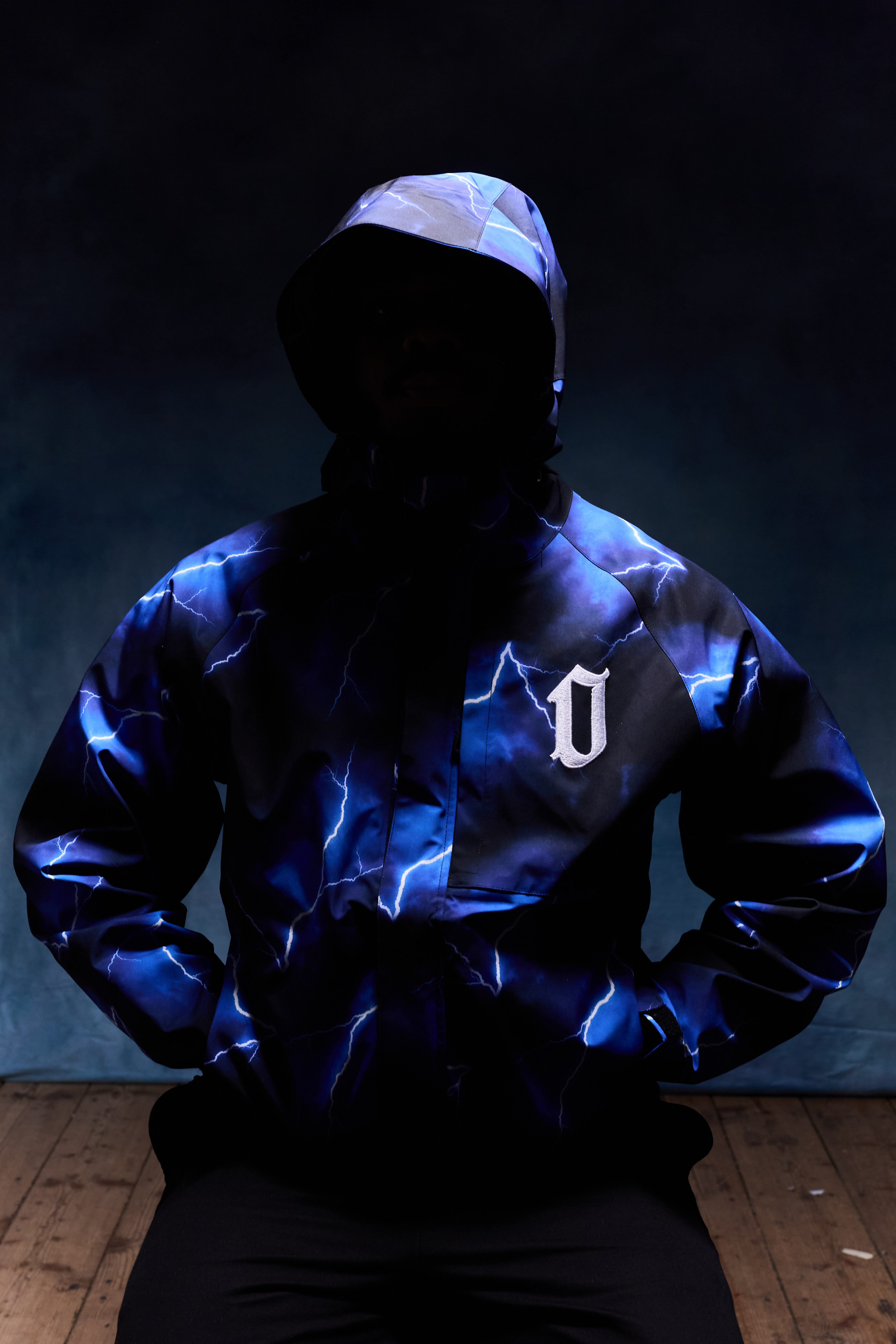 Person wearing a hooded jacket with a blue lightning pattern and a white letter 'U' emblem on the chest.
