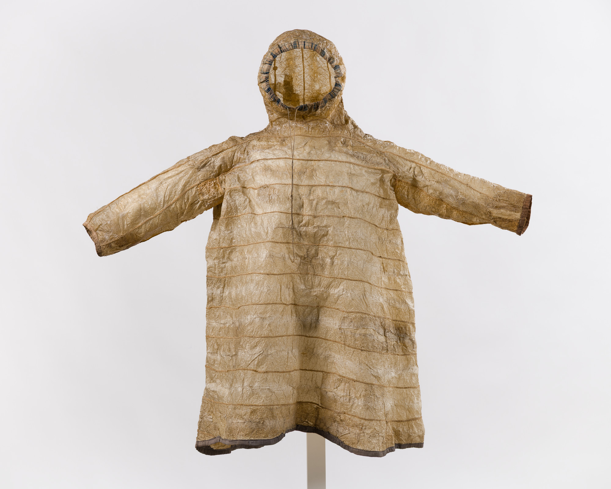 Traditional translucent brown seal skin parka with hood and outstretched arms displayed on a stand.