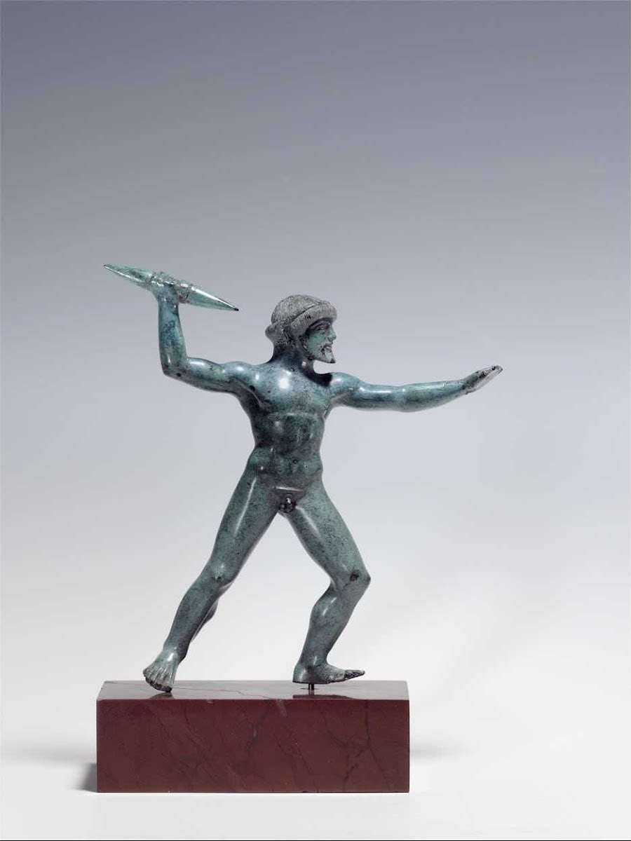 Ancient bronze statue of a naked male warrior wearing a helmet, poised to throw a spear, standing on a red marble base.