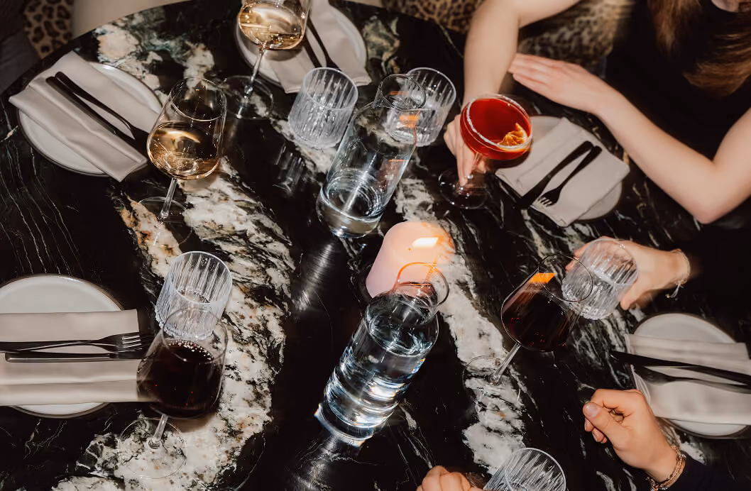 Top view of three people at a marble table with wine glasses, water glasses, plates, and a lit candle.