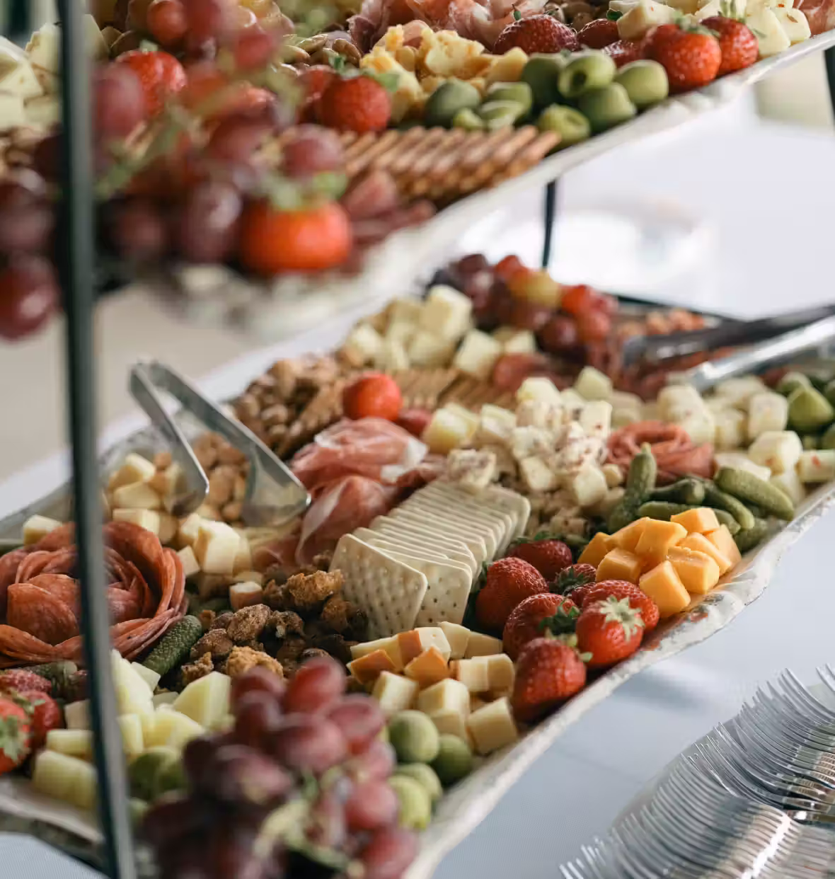 Two-tiered platter with an assortment of cheese cubes, strawberries, crackers, meats, grapes, pickles, and nuts, arranged for serving.
