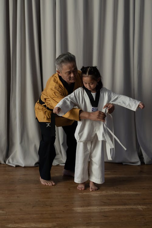 A martial arts instructor helps a young student with a white belt during a grading ceremony in a dojo