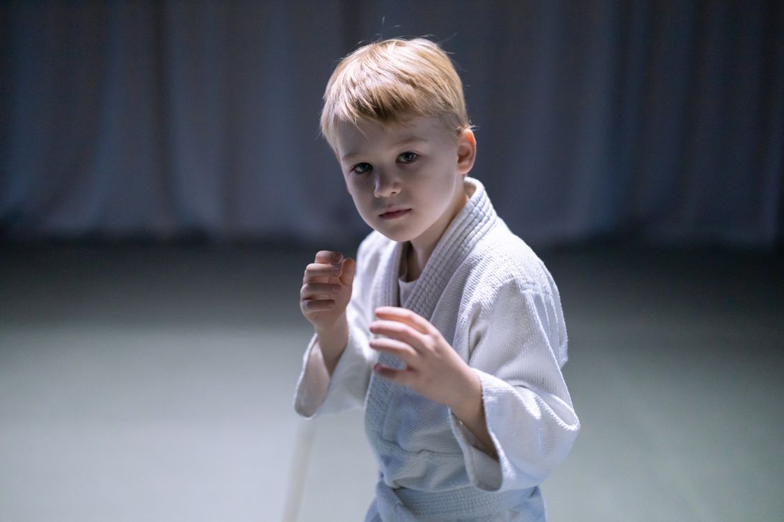 A young boy in a white gi holding a focused guard stance during a beginner martial arts class