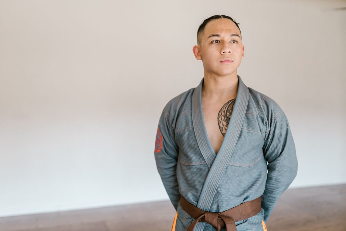An adult martial artist in a grey gi wearing a brown belt, representing advanced rank progression and the visible path to the next level