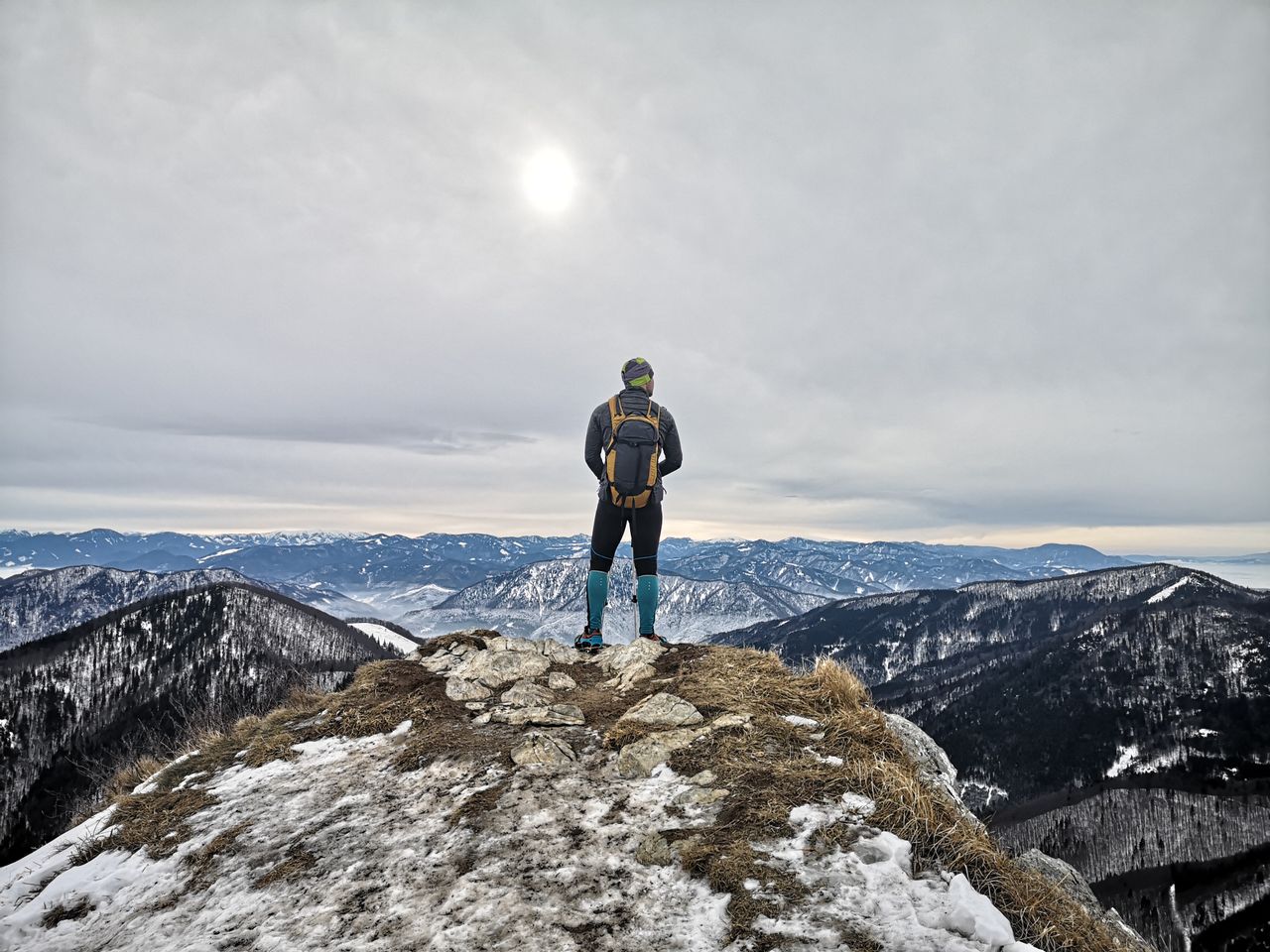 A person with a backpack stands on a snowy mountain summit, gazing at other peaks, representing new goals and challenges.