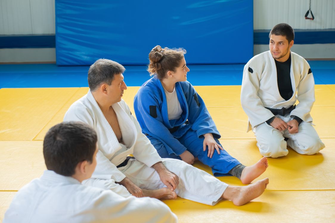 Judo students of different ages sitting together on the mat and talking between drills
