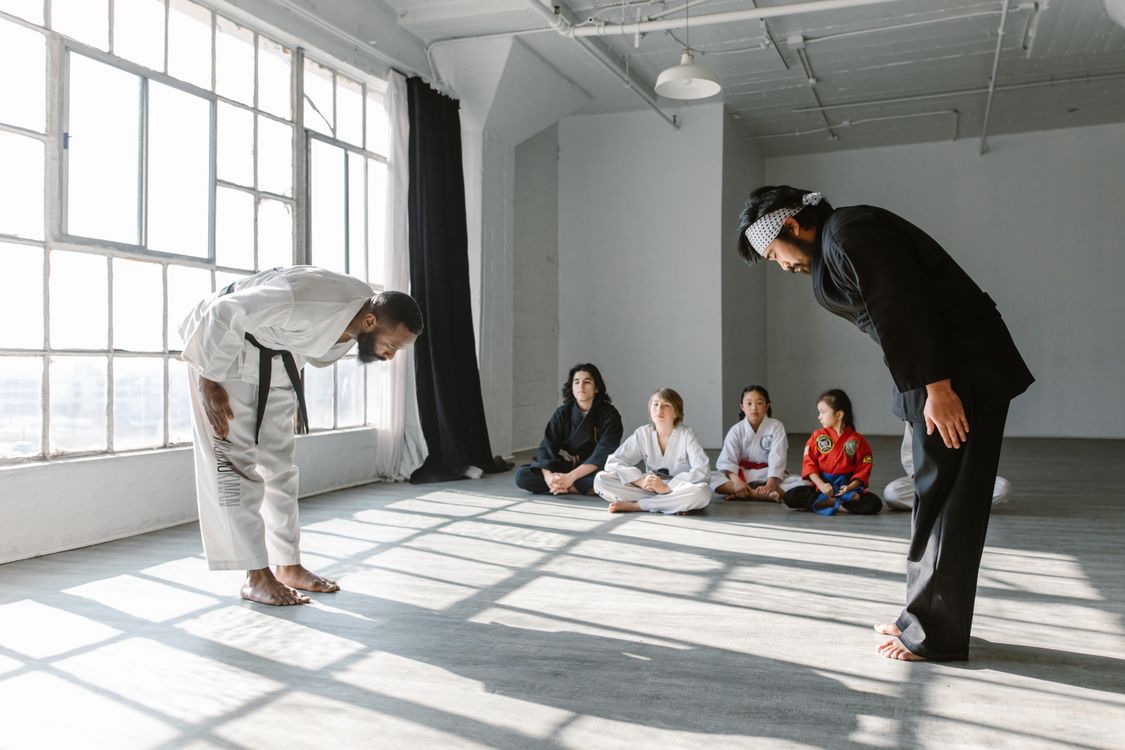 Students and instructors bow at the start of a martial arts class in a small dojo