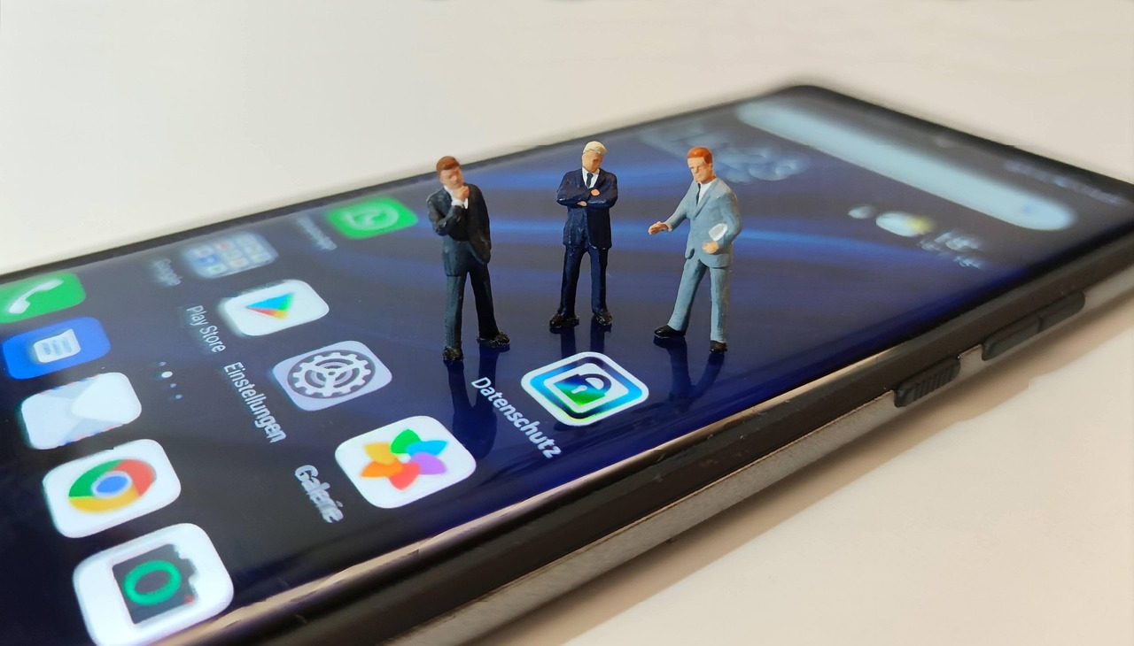 Smartphone-Bildschirm mit dem deutschen App-Symbol Datenschutz neben Einstellungen und Galerie, darauf drei Miniaturfiguren im Anzug