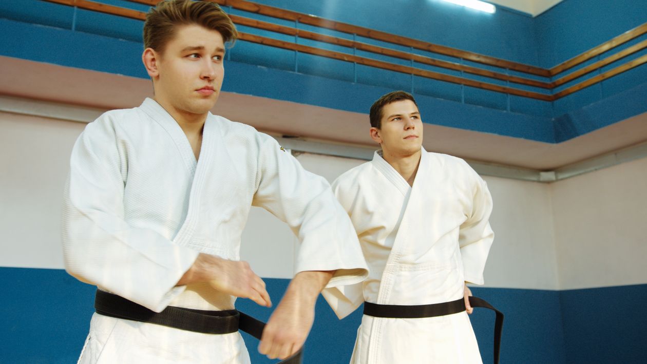 Zwei Kampfsportler mit schwarzen Gürteln trainieren gemeinsam in der Halle
