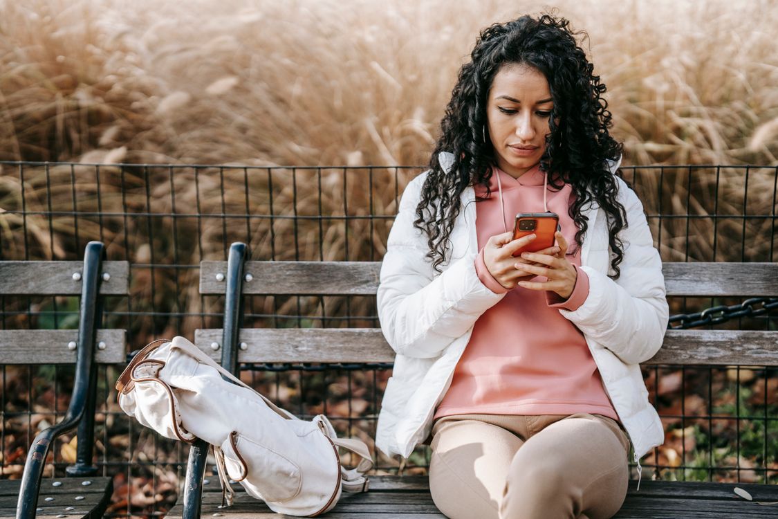 A woman sitting on a park bench reading a message on her phone