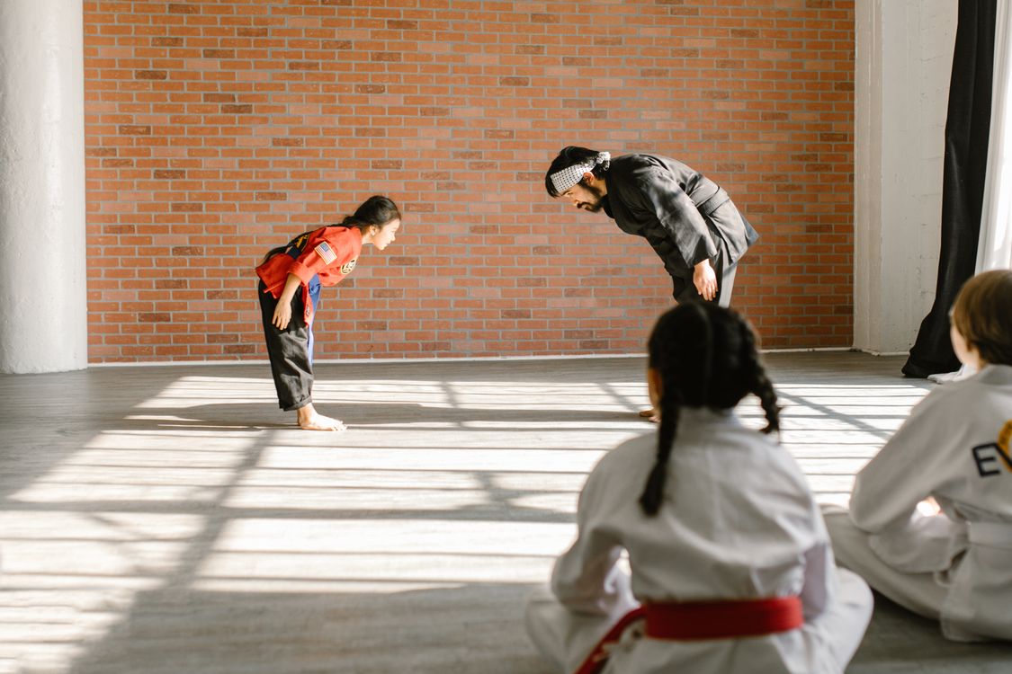 A martial arts instructor and a young student bowing to each other in a sunlit dojo