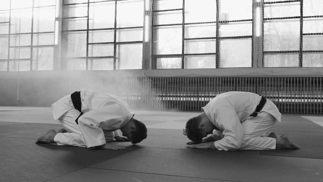 Two martial artists kneeling in a formal bow on the mat of a training hall