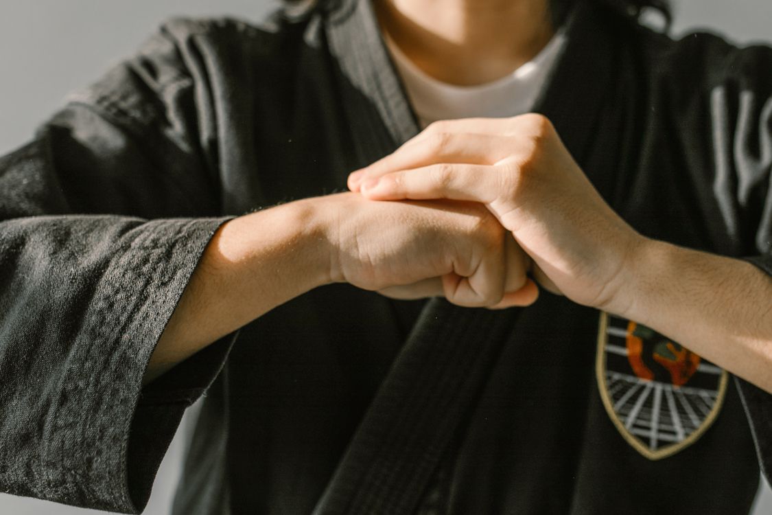 A martial artist in a black gi making a fist-and-palm salute