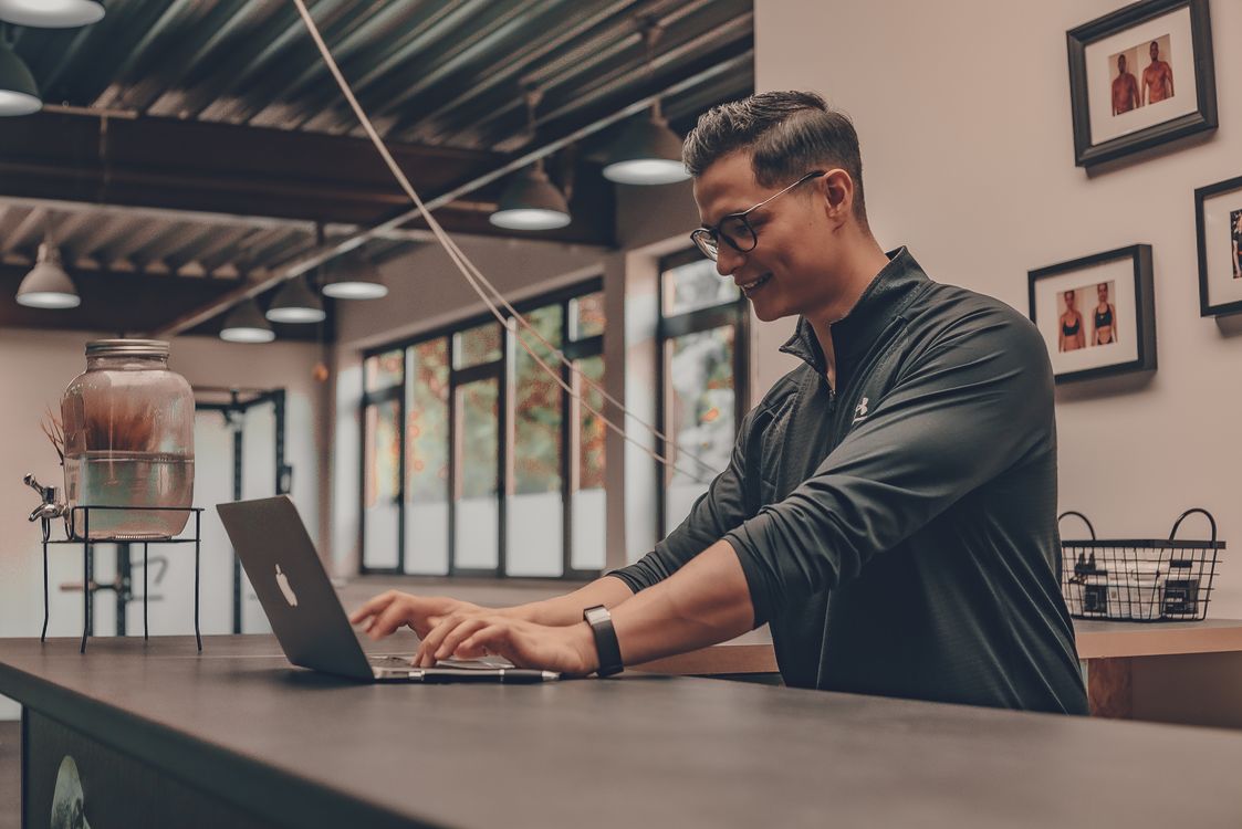 A martial arts instructor in sportswear checks class records on a laptop at the reception counter of a training hall