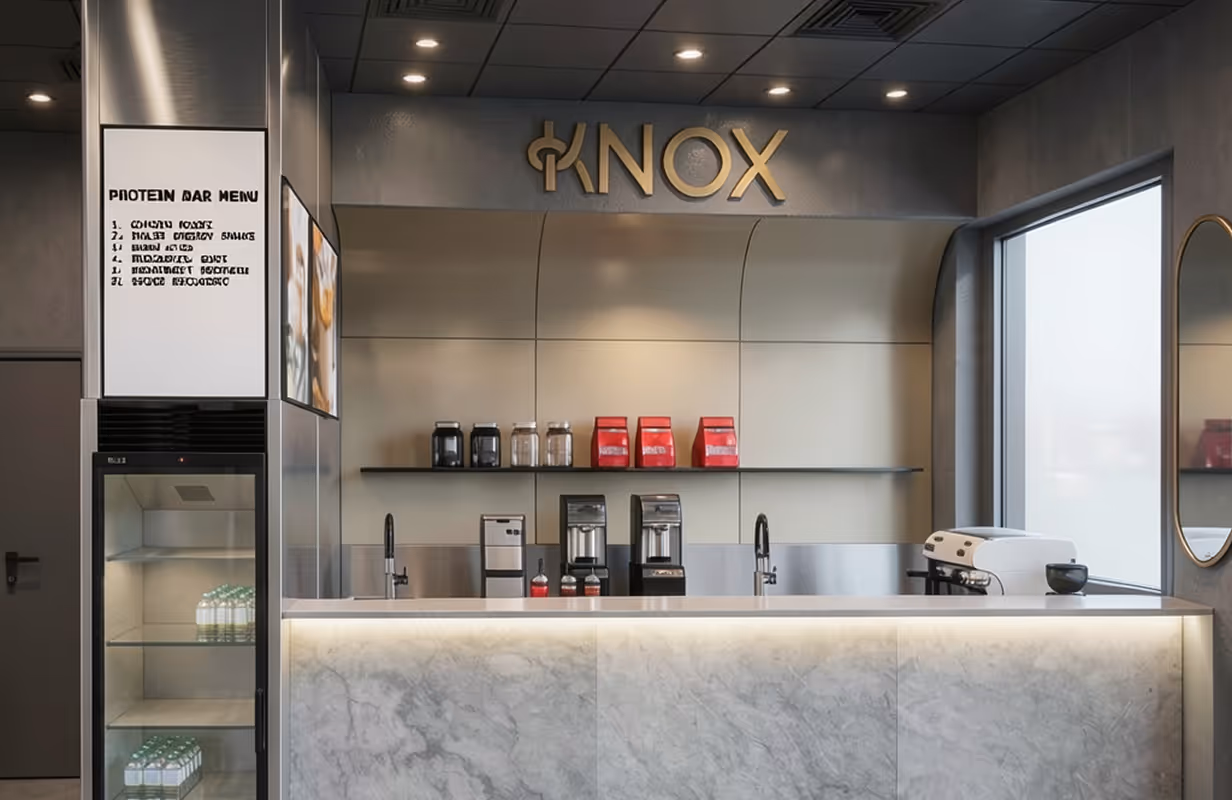 Nowoczesny bar białkowy z marmurowym blatem, ekspresami do kawy i lodówką ze schłodzonymi butelkami wody.