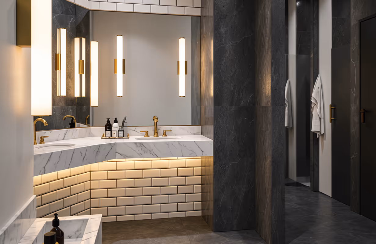 Nowoczesna łazienka z podwójną umywalką z marmuru, złotymi bateriami i podświetlanym panelem z białych płytek.