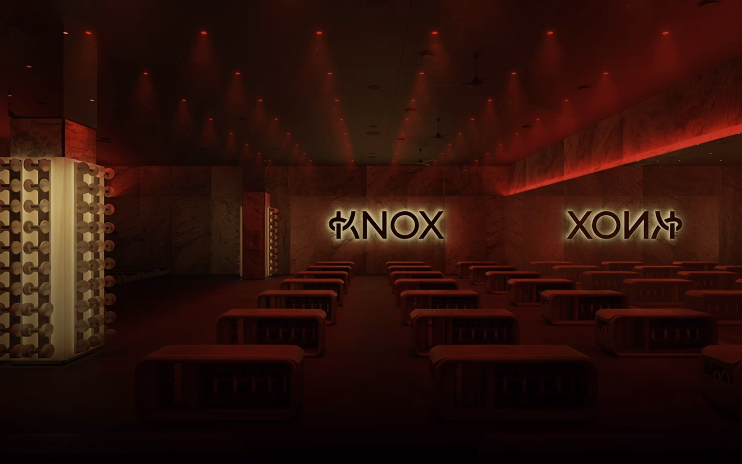 Wnętrze sali fitness z czerwonym oświetleniem i rzędami ławek, na ścianie podświetlony napis KNOX.