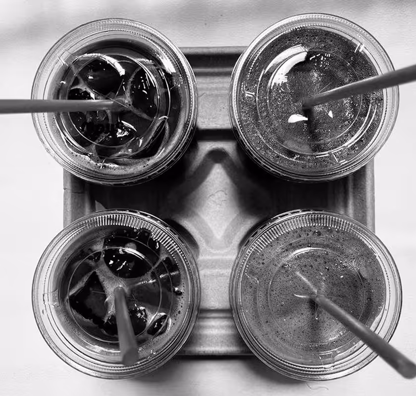 Widok z góry na cztery plastikowe kubki z zimnym napojem z lodem i słomkami ułożone w kartonowym uchwycie.