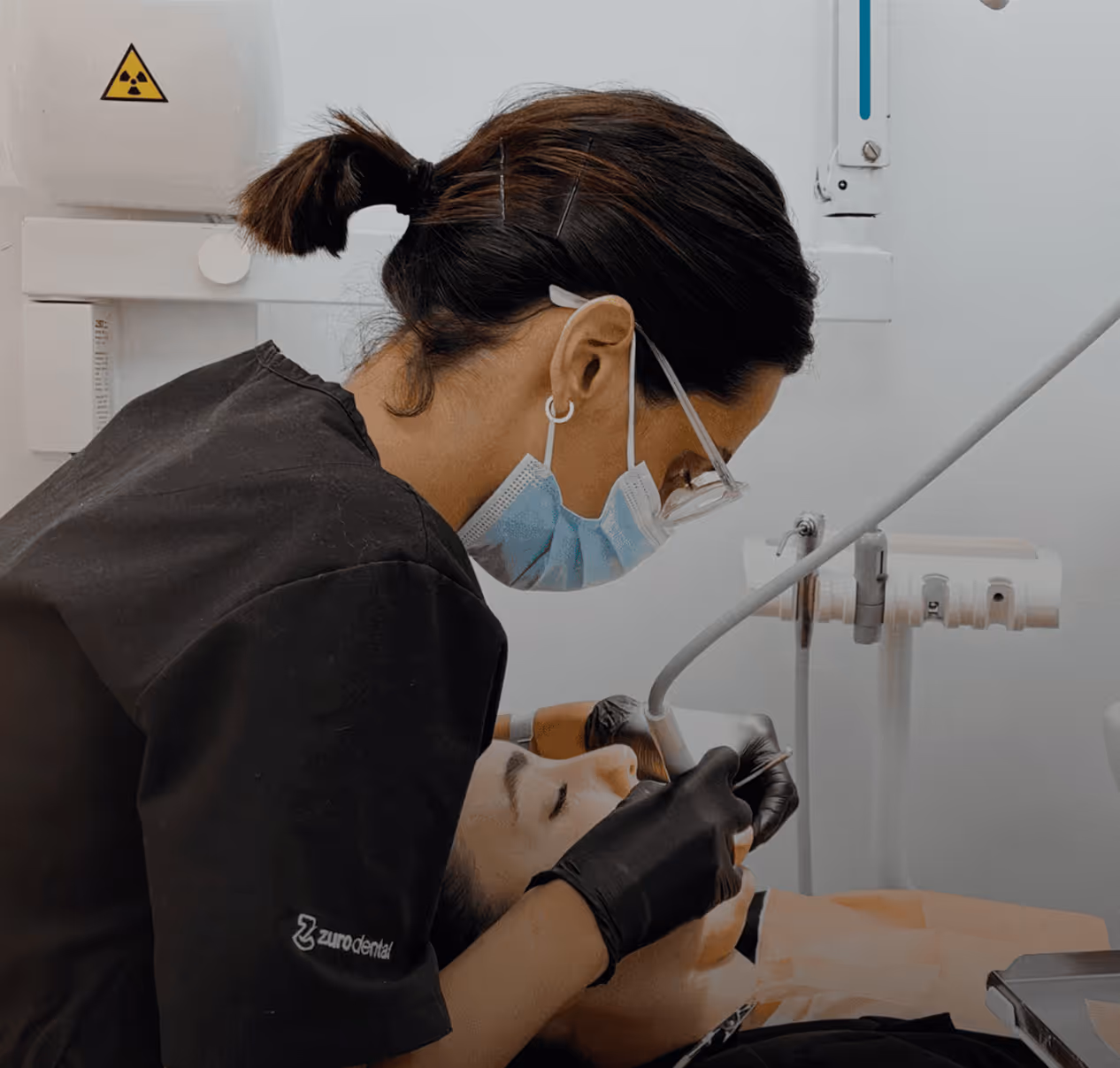 Dentista con guantes y mascarilla realizando un tratamiento dental a un paciente reclinado.