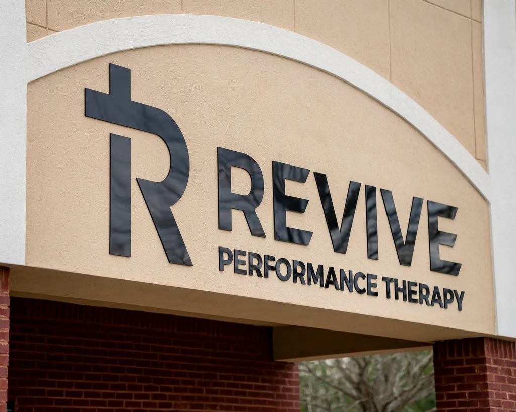Exterior sign reading 'Revive Performance Therapy' with a stylized R logo on a beige building facade.