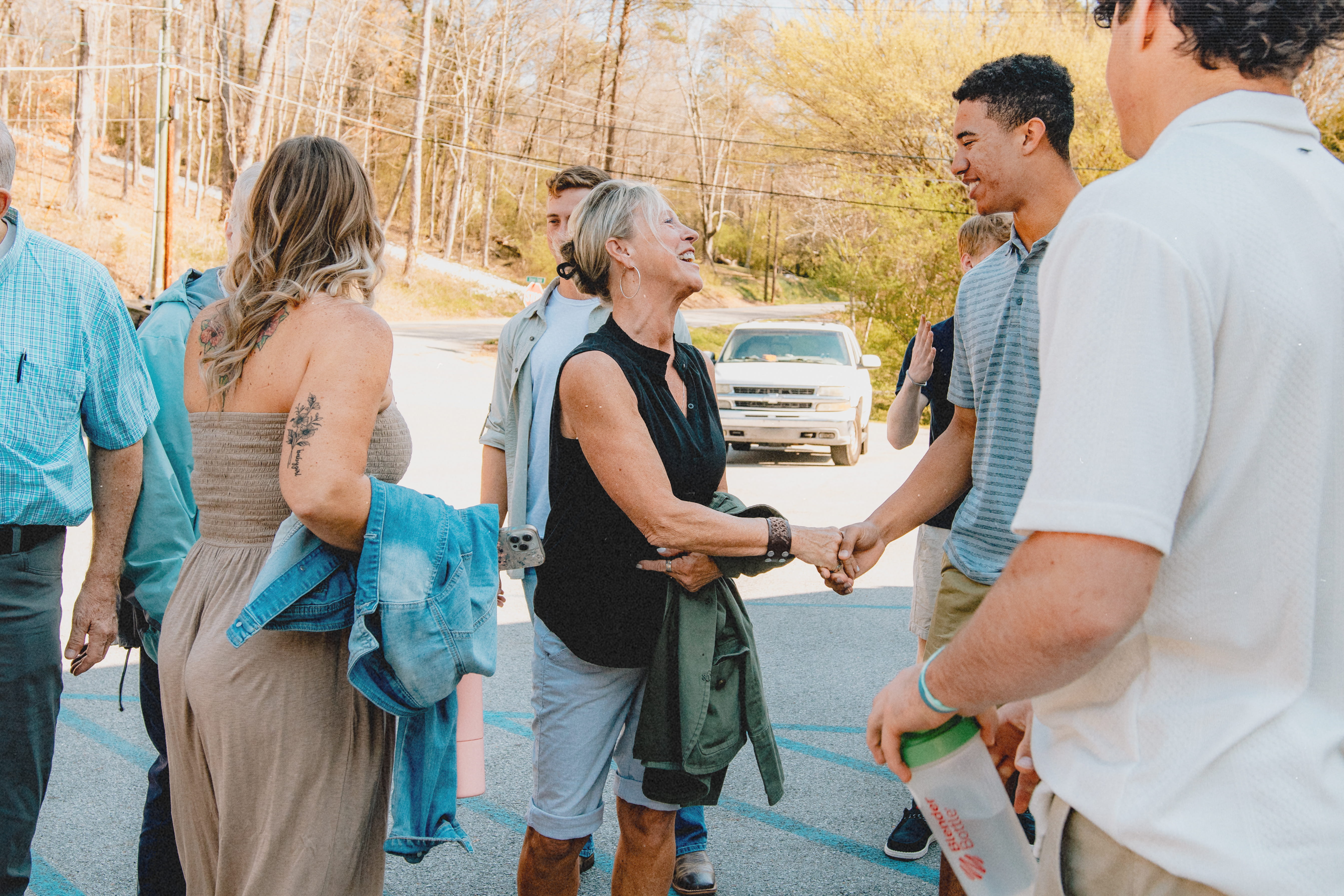 Members of the congregation outdoors greeting and shaking hands with smiles in a sunny setting.