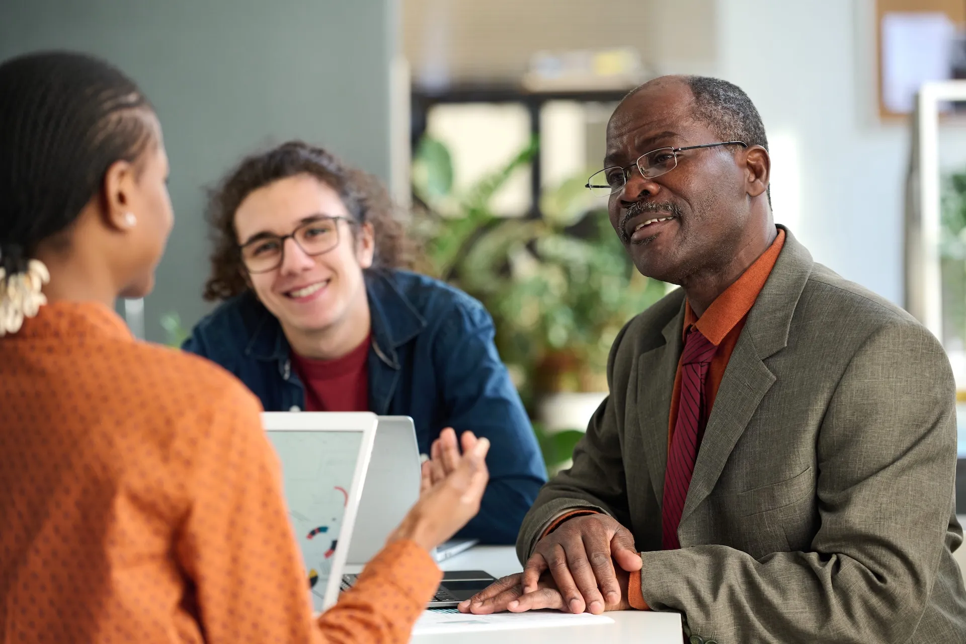 Three professionals in an office having a discussion with a laptop and tablet.