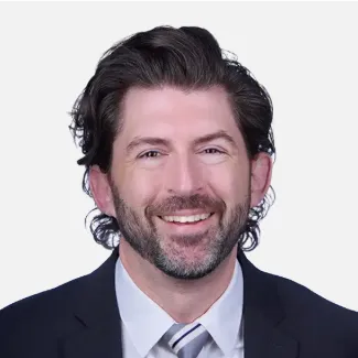 Professional headshot of a smiling man with dark hair and beard wearing business attire.