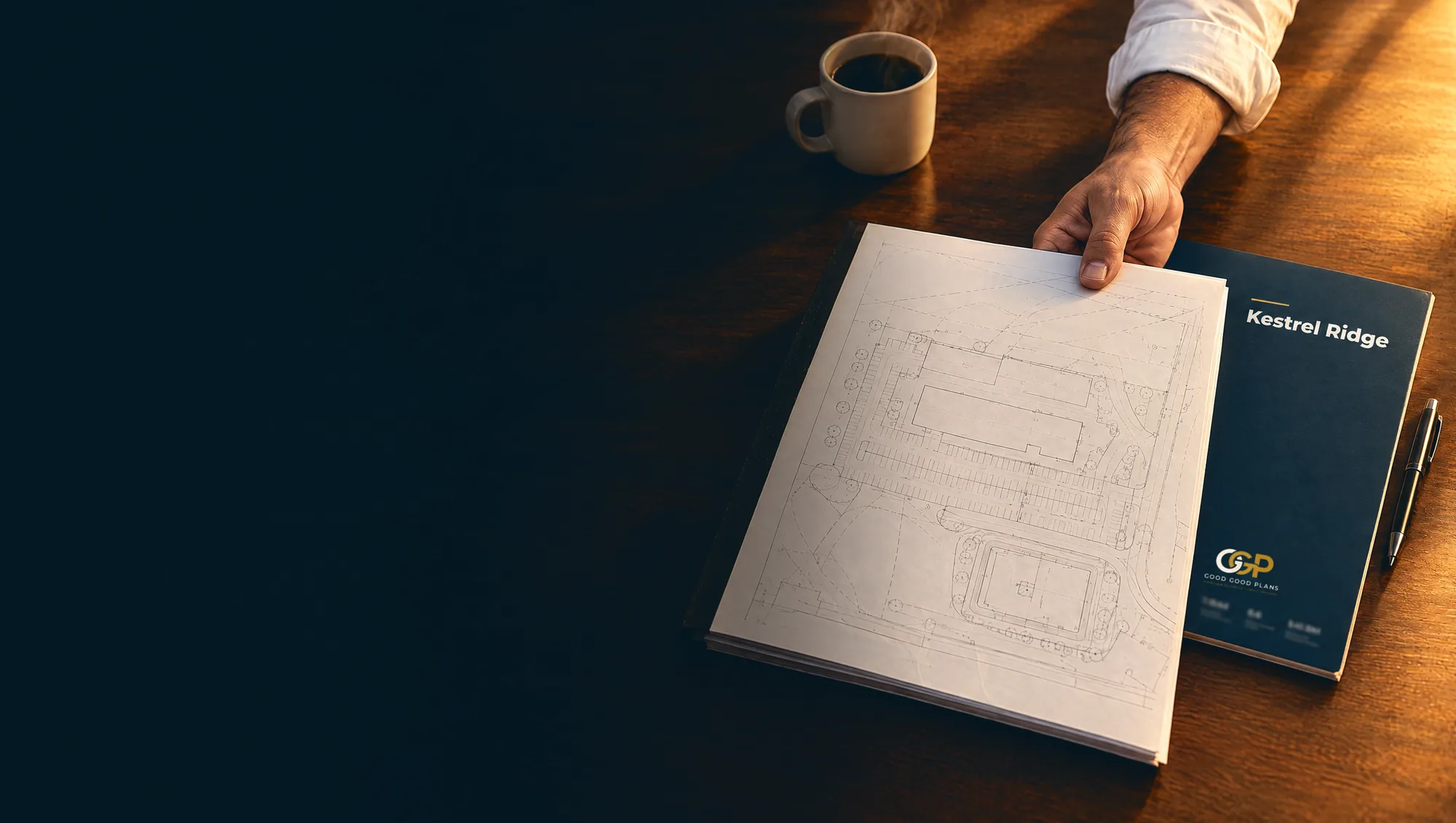 A hand passing a set of drawings across a table beside a Good Good Plans design review