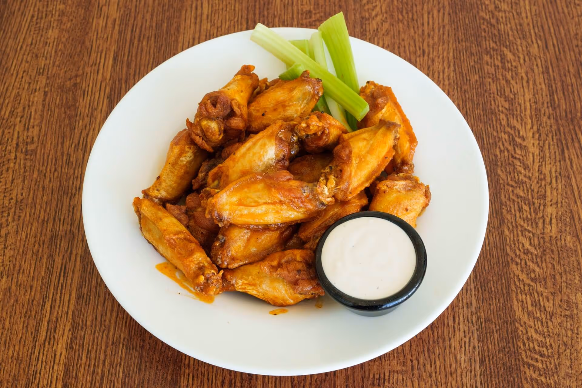 Plate of crispy buffalo chicken wings served with celery sticks and a cup of ranch dipping sauce on a wooden table.