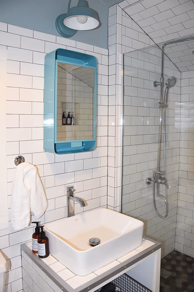Modern bathroom with white subway tiles, a white rectangular sink, chrome faucet, blue-framed mirror, wall-mounted light, and a glass-enclosed shower.