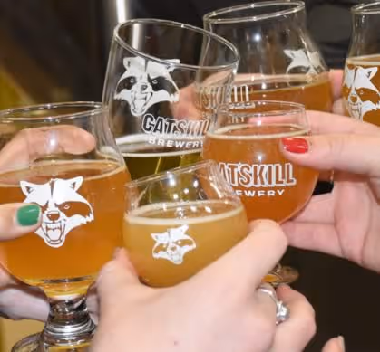 Hands clinking glasses of beer with Catskill Brewery logo on the glasses.