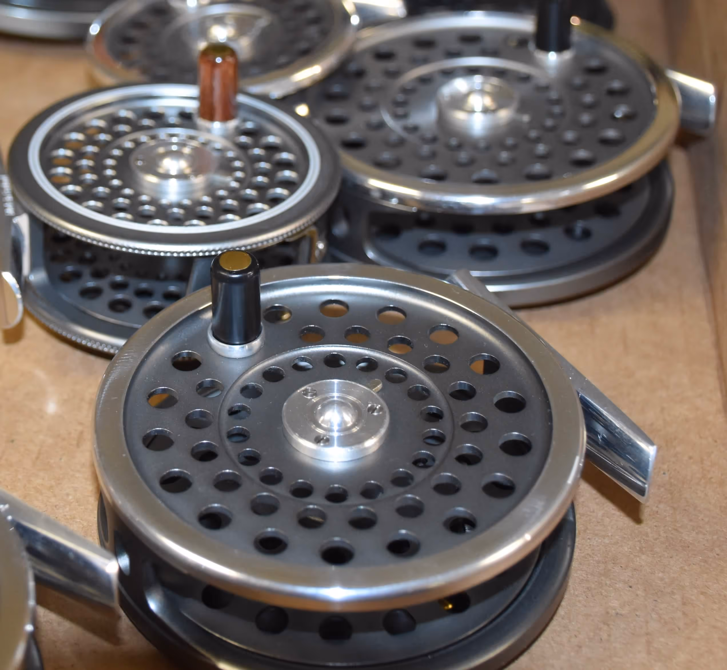 Close-up of several metal fly fishing reels with perforated circular designs on a wooden surface.