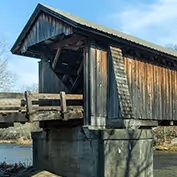 Covered wooden bridge over a calm river with a clear blue sky in the background.