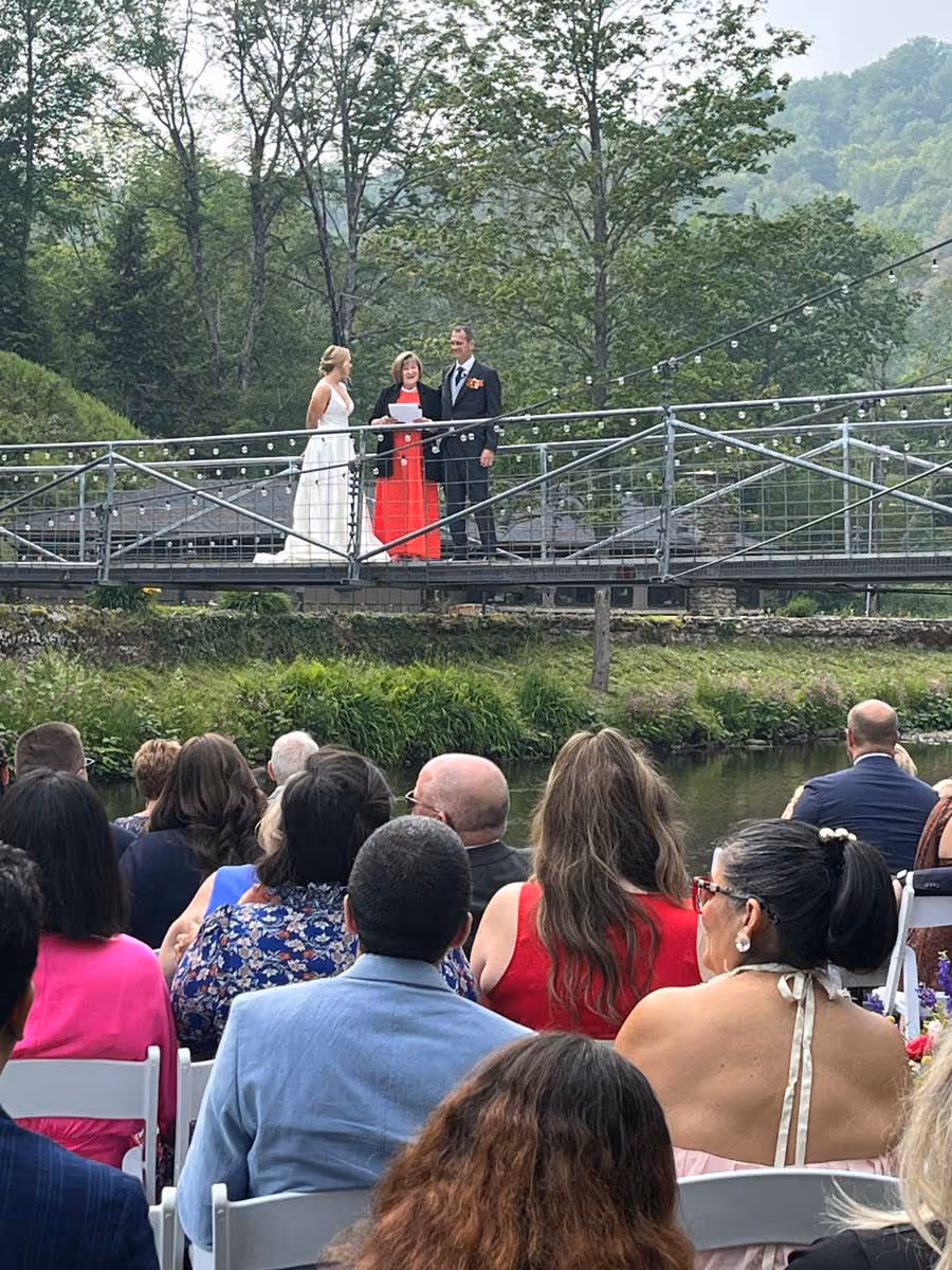 Wedding ceremony on a decorated outdoor bridge with bride, groom, officiant, and seated guests.