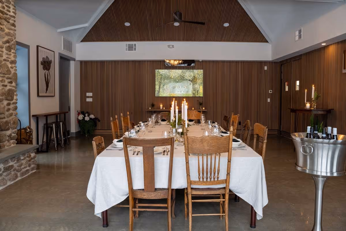 Elegant dining room with a long table set for a dinner, wooden chairs, candles, and a wine cooler.