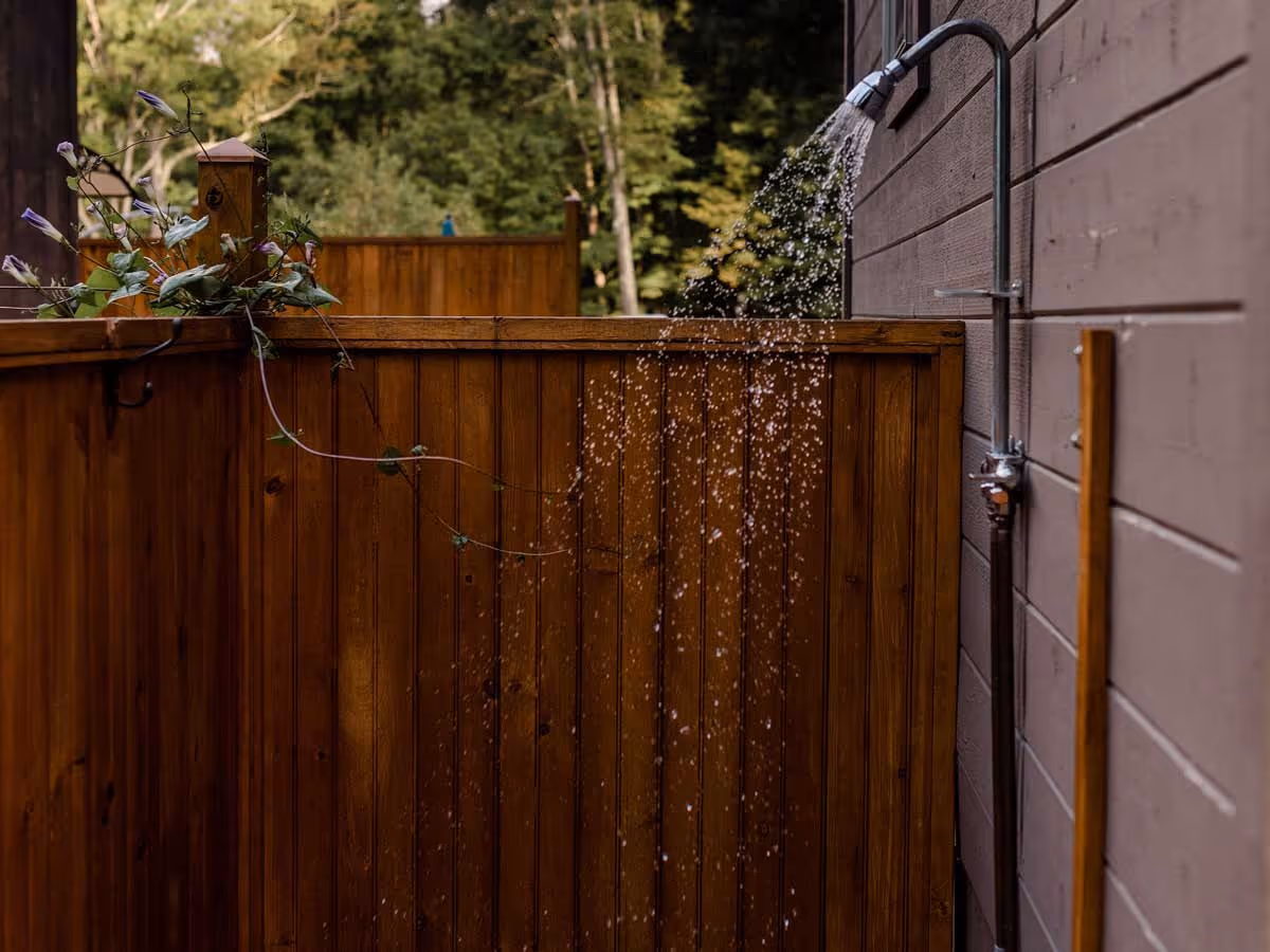 Outdoor shower with water flowing from the showerhead mounted on a wooden fence wall.
