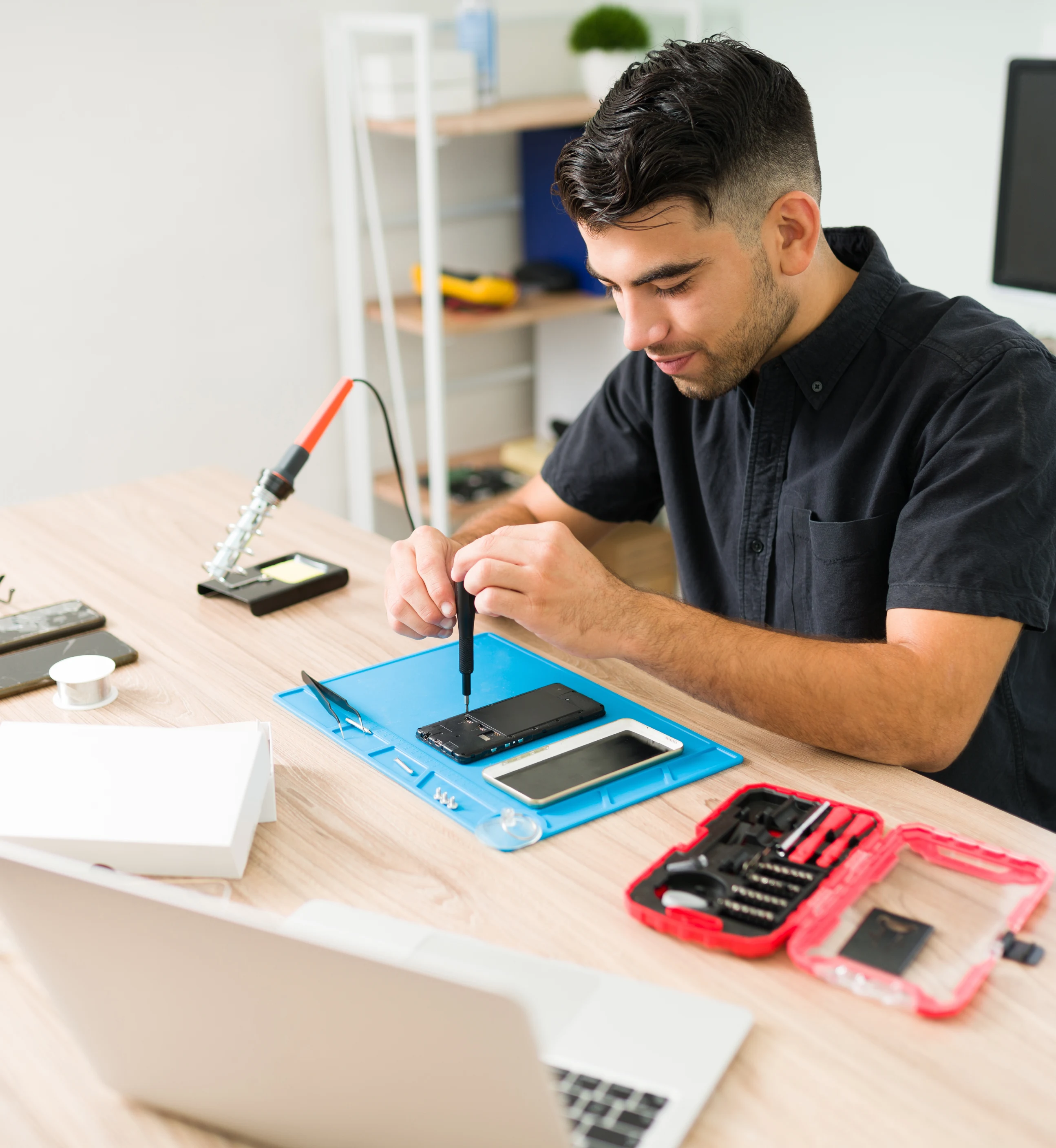 Technician repairing a phone at a workbench with tools laid out